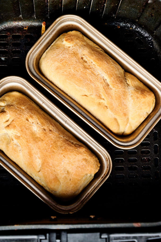 Two golden-brown loaves of Air Fryer Sourdough Focaccia rest in metal loaf pans inside an air fryer basket.