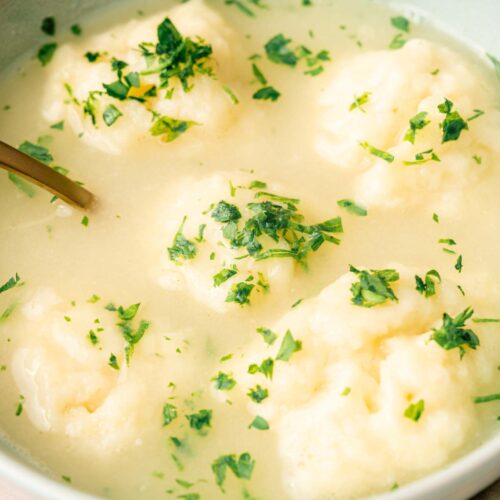 A bowl of clear soup with several dumplings, garnished with chopped fresh herbs for a delightful dumplings experience.