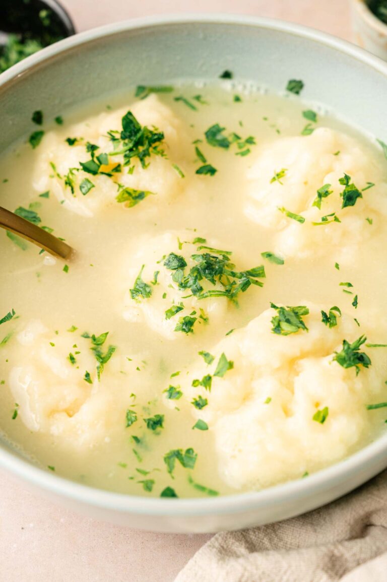 A bowl of clear soup with several dumplings, garnished with chopped fresh herbs for a delightful dumplings experience.