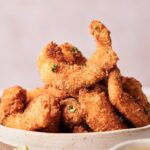 A bowl filled with golden-brown, breaded and fried coconut shrimp, garnished with chopped parsley.