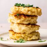 A stack of four golden-brown Irish Potato pancakes garnished with chopped herbs, served on a white plate.