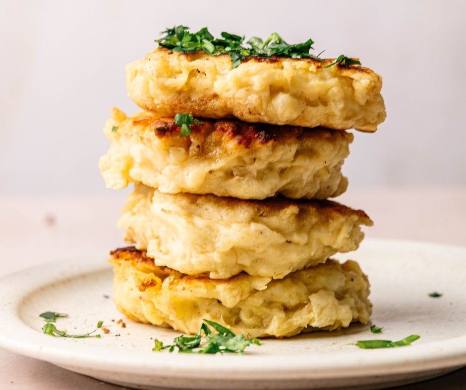 A stack of four golden-brown Irish Potato pancakes garnished with chopped herbs, served on a white plate.
