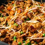 Close-up of Pork Fried Rice with diced pork, carrots, peas, scrambled eggs, and bean sprouts in a pan.