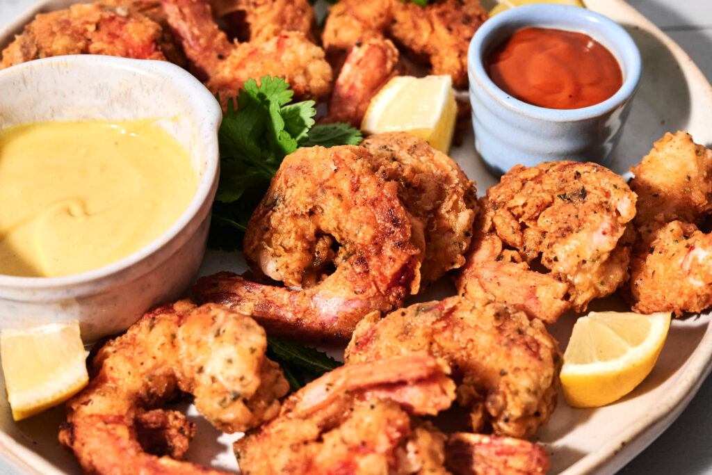Plate of crispy fried shrimp served with lemon wedges, parsley, and two dipping sauces&mdash;one yellow and one red.