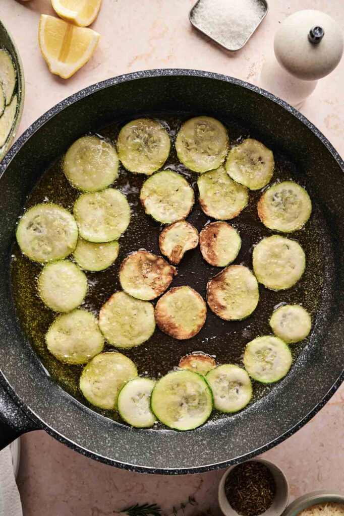 A pan of fried zucchini sizzles as it cooks, filling the kitchen with a tempting aroma.