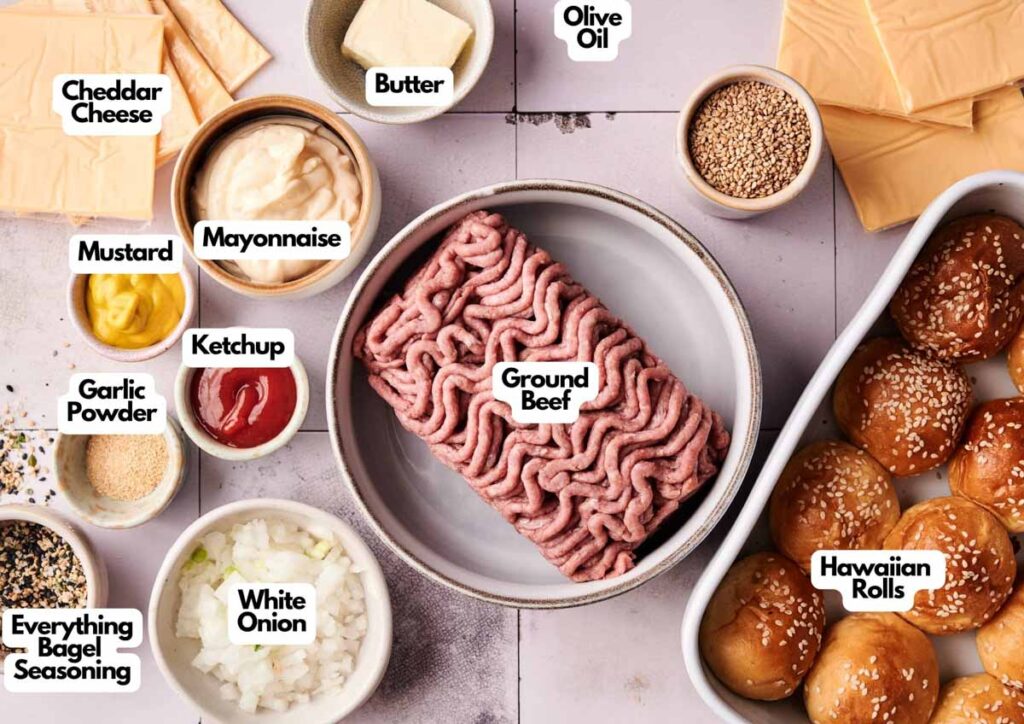 Top-down view of Air Fryer Hamburger Slider ingredients, including ground beef, cheddar cheese, Hawaiian rolls, condiments, spices, butter, olive oil, and diced onion&mdash;all clearly labeled.