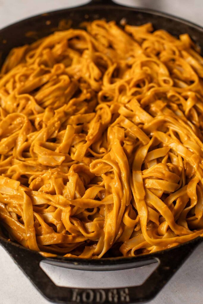 A cast iron pan filled with Hidden Veggie Pasta—fettuccine coated in a creamy orange sauce that sneaks in extra nutrition without sacrificing flavor.