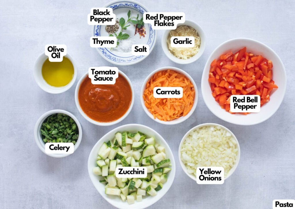 Bowls with labeled ingredients for Hidden Veggie Pasta, including tomato sauce, garlic, olive oil, thyme, black pepper, salt, red pepper flakes, carrots, red bell pepper, yellow onions, celery, and zucchini.