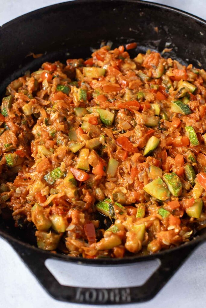 Chopped vegetables including zucchini, tomatoes, and onions are cooked in a black cast iron skillet, perfect for adding to your favorite Hidden Veggie Pasta.