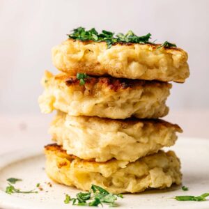 A stack of four golden, crispy Irish Potato pancakes garnished with chopped herbs on a white plate.