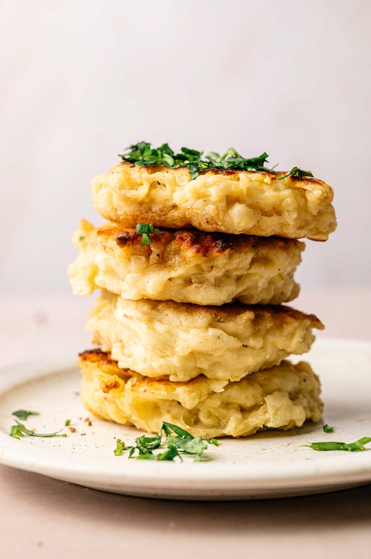 A stack of four golden, crispy Irish Potato pancakes garnished with chopped herbs on a white plate.