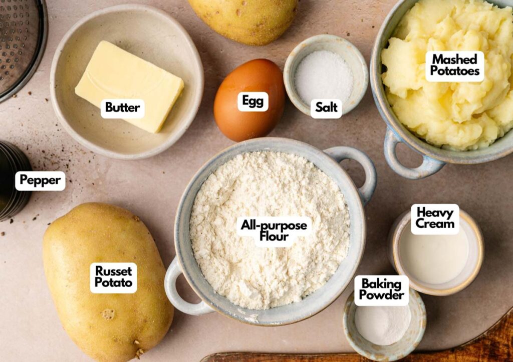 Top-down view of labeled ingredients for an Irish Potatoes recipe, including butter, egg, salt, mashed potatoes, heavy cream, baking powder, all-purpose flour, russet potato, and pepper.