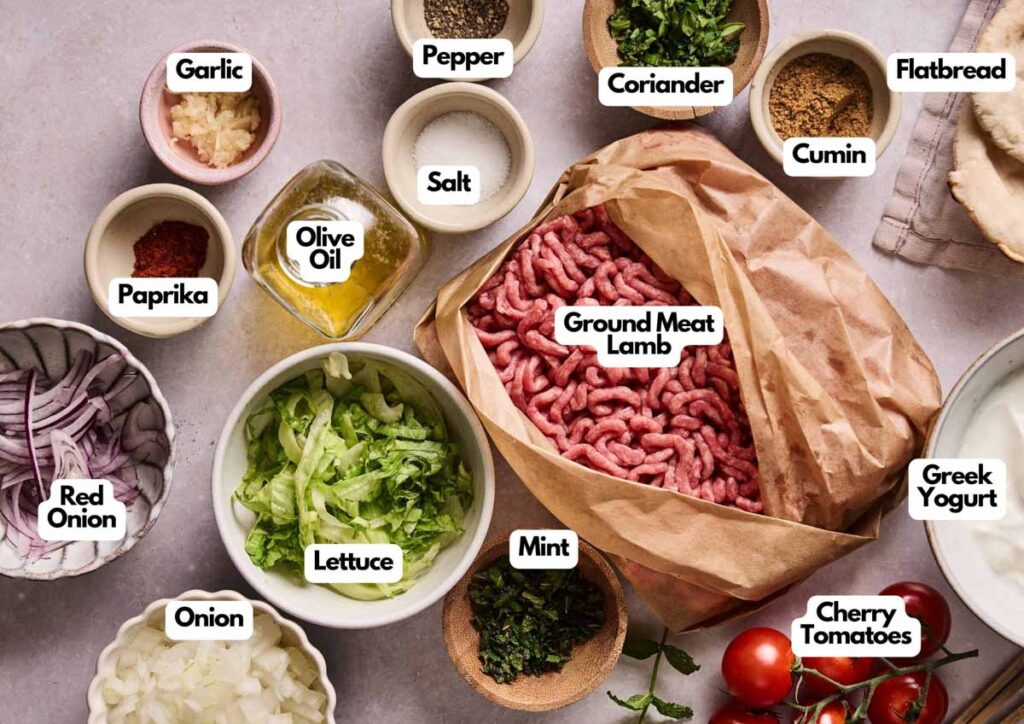 Various labeled ingredients for lamb flatbreads and Lamb Kebabs, including ground meat, spices, vegetables, yogurt, olive oil, and flatbread, arranged on a countertop.