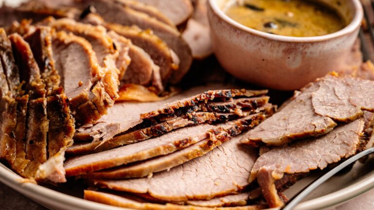 Sliced roast beef arranged on a plate with a bowl of gravy or sauce on the side.