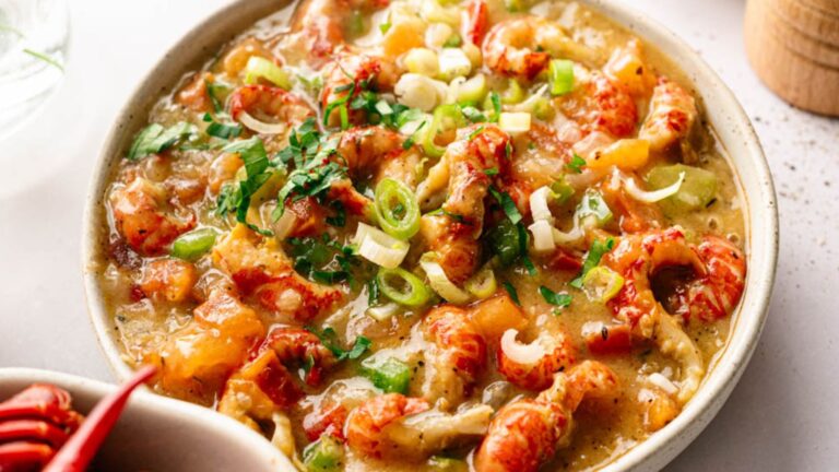 A bowl of crawfish étouffée topped with chopped green onions and herbs, featuring a thick, seasoned sauce and visible pieces of crawfish.