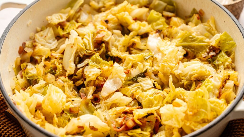 Chopped cooked cabbage mixed with sautéed onions in a white pot.