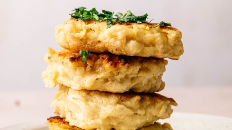 Three golden brown fritters stacked on a plate, topped with chopped green herbs.