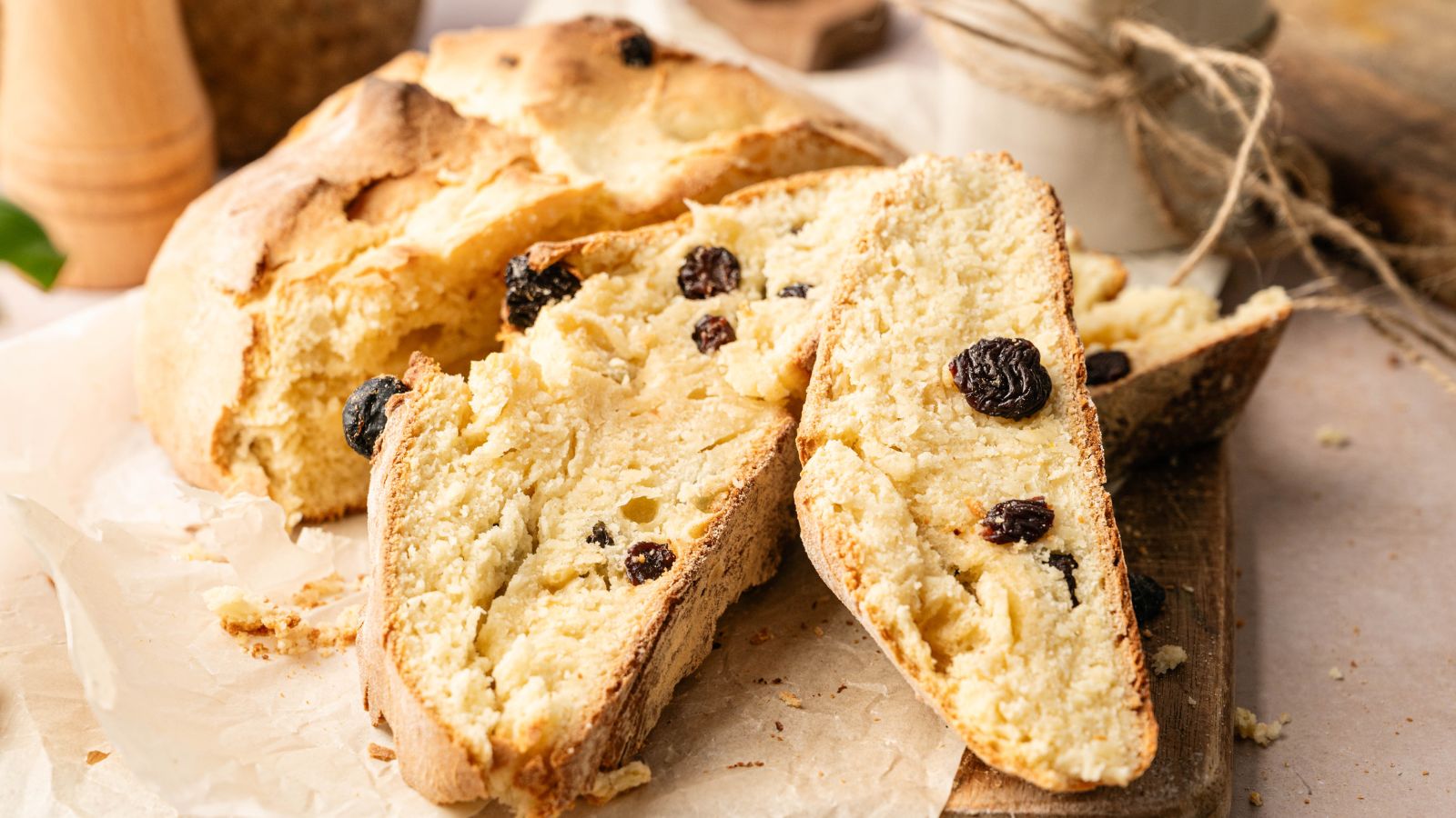 Sliced loaf of rustic bread with raisins on a wooden board and parchment paper.