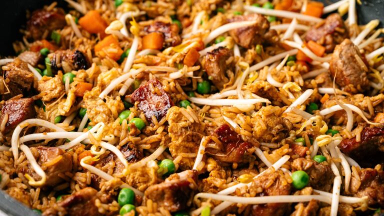 Close-up of fried rice with chunks of meat, peas, carrots, and bean sprouts.