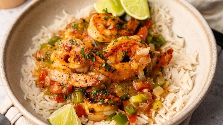 A bowl of cooked shrimp with chopped vegetables and sauce served over white rice, garnished with lime wedges.