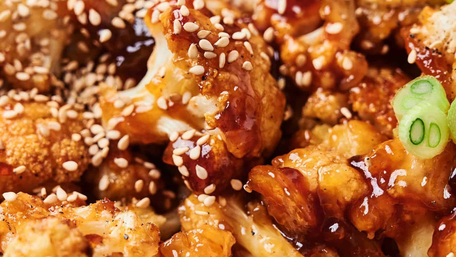 Close-up of Sticky Sesame Cauliflower: crispy florets coated in a glossy sauce, garnished with sesame seeds and sliced green onions.