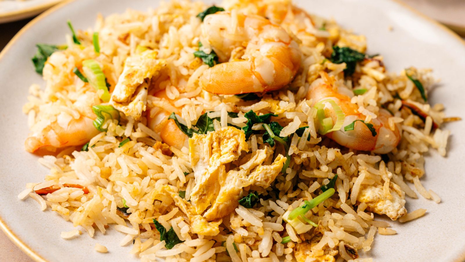 A plate of shrimp fried rice with pieces of scrambled egg, green onions, and leafy vegetables.