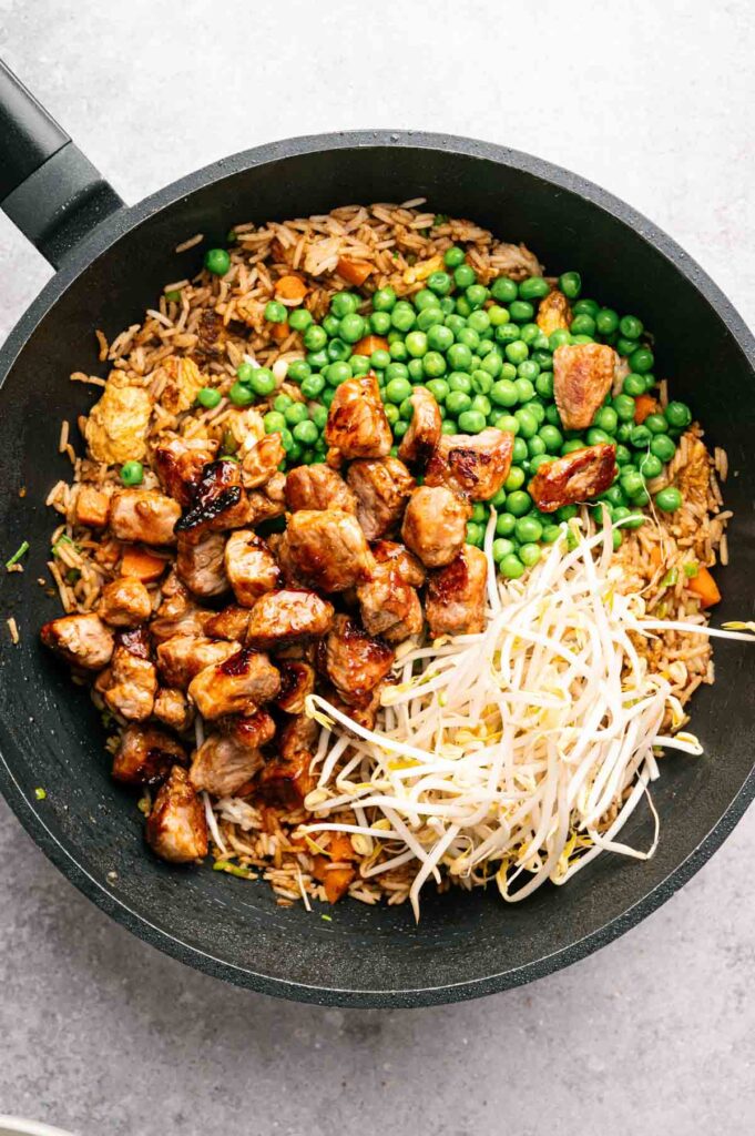 A pan filled with Pork Fried Rice, featuring green peas, cooked pork pieces, and fresh bean sprouts.
