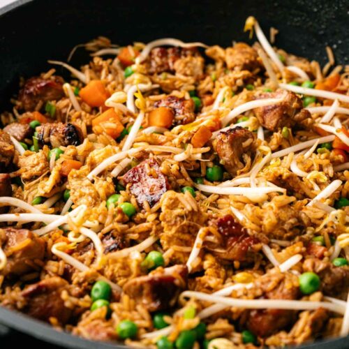 A skillet filled with Pork Fried Rice, featuring chunks of meat, peas, carrots, and bean sprouts.