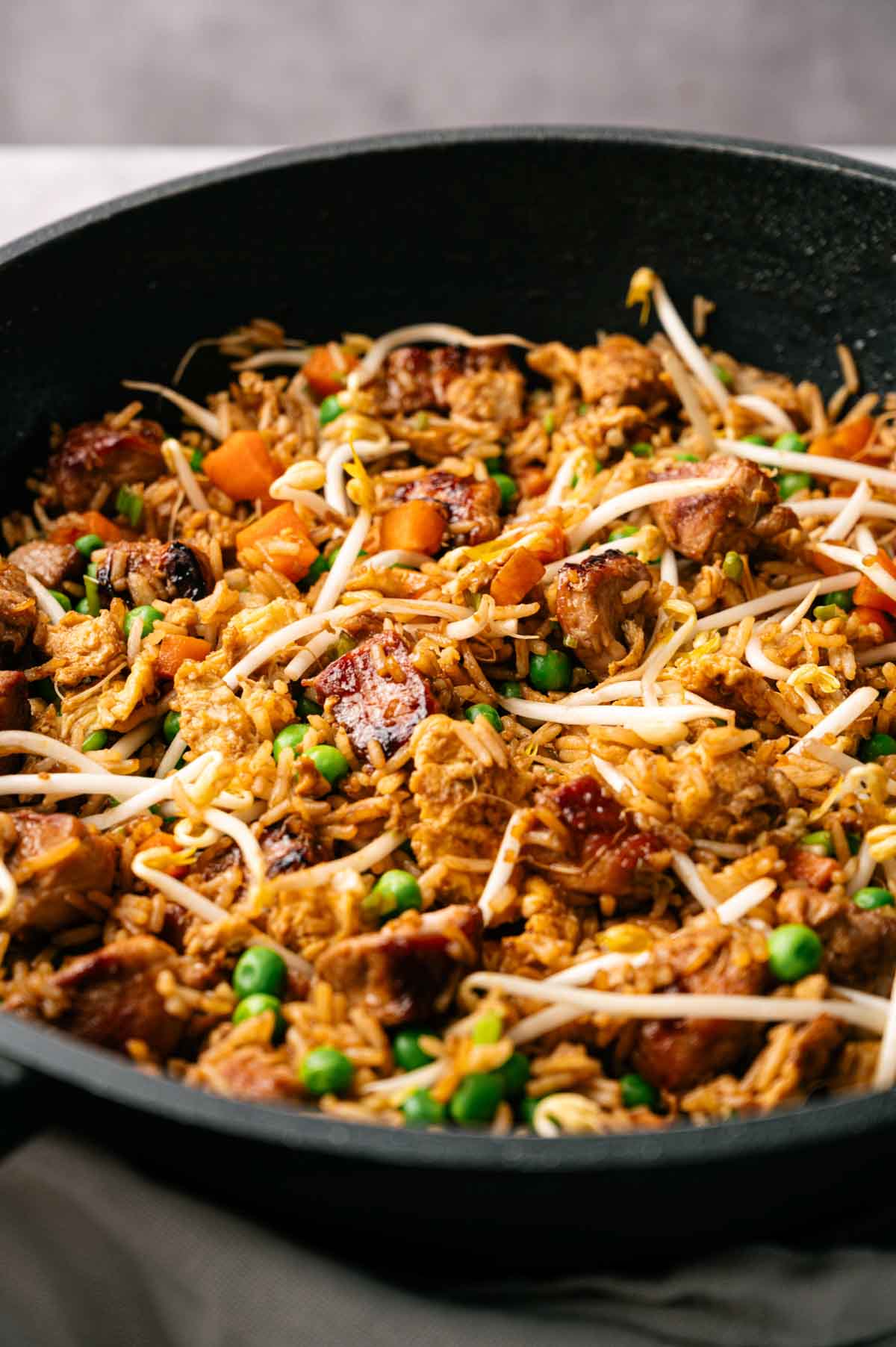 A skillet filled with Pork Fried Rice, featuring chunks of meat, peas, carrots, and bean sprouts.