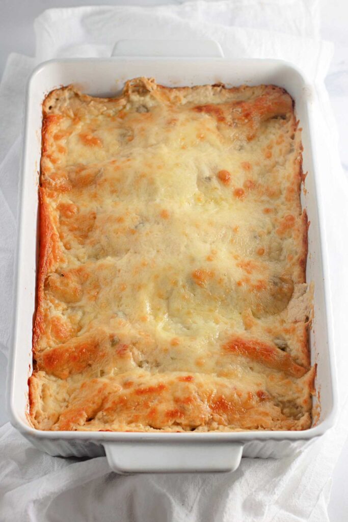 A baked White Chicken Enchiladas casserole with a golden, melted cheese topping in a white rectangular dish on a white cloth.