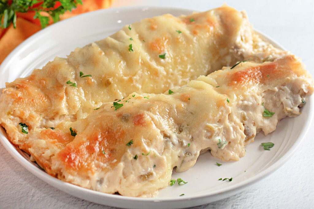 Two creamy, cheese-topped White Chicken Enchiladas garnished with chopped parsley on a white plate.