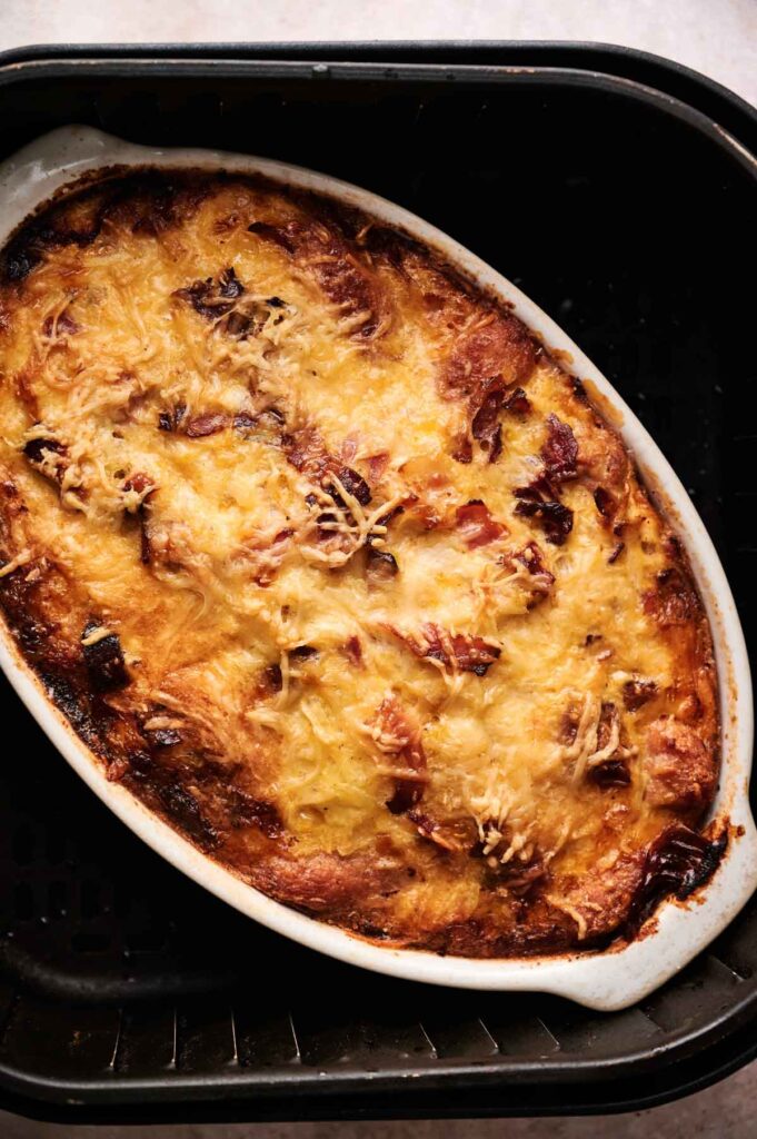 An Air Fryer Amish Breakfast Casserole baked to perfection, topped with melted cheese and browned edges, served in an oval white dish.
