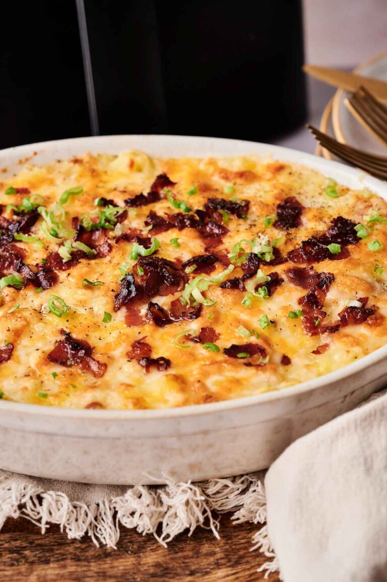An Air Fryer Twice Baked Potato Casserole topped with melted cheese, crispy bacon pieces, and chopped green onions in a round ceramic dish.