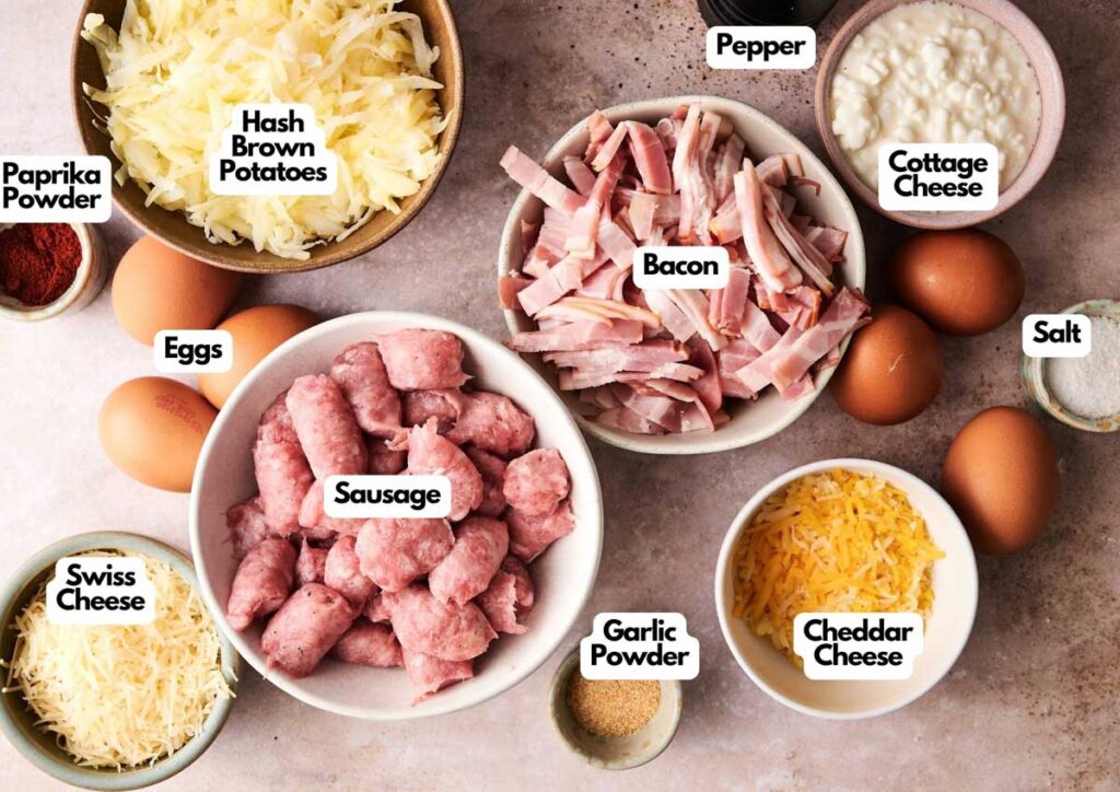 Air Fryer Amish Breakfast Casserole bowls filled with hash brown potatoes, bacon, sausage, eggs, Swiss and cheddar cheese, cottage cheese, paprika powder, garlic powder, salt, and pepper on a countertop.