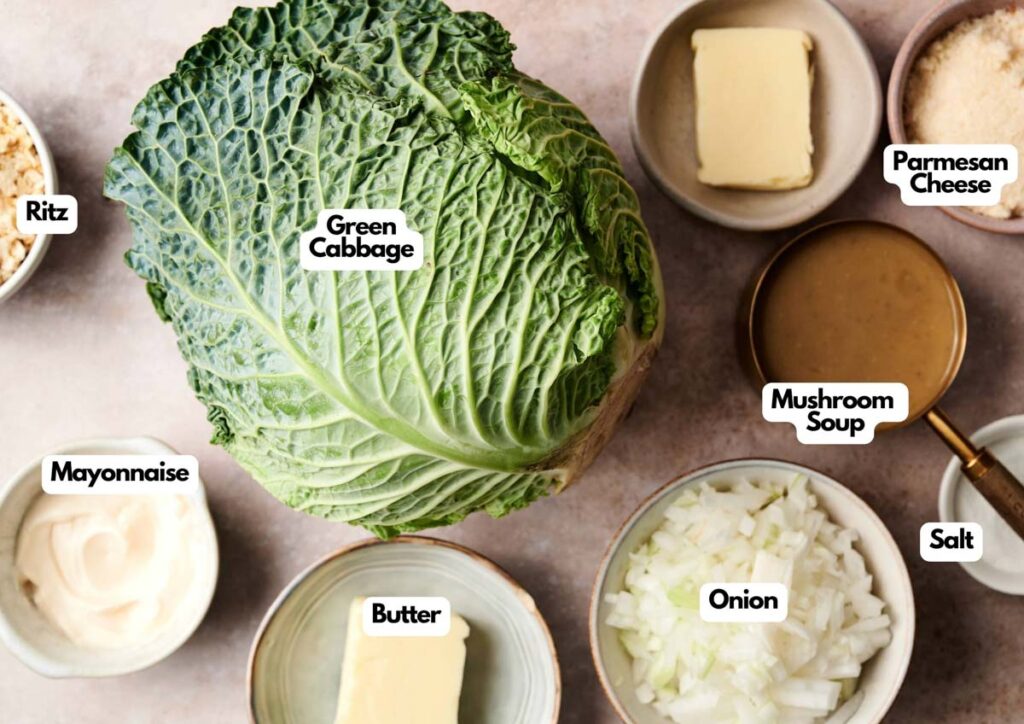 Top-down view of labeled ingredients for Air Fryer Cabbage Casserole, including a head of green cabbage, mayonnaise, butter, chopped onion, salt, mushroom soup, Parmesan cheese, and Ritz crackers.