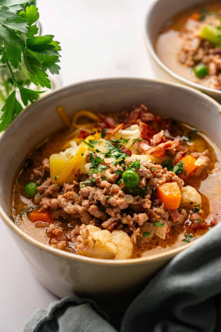 A hearty bowl of Cheeseburger Soup with ground meat, peas, carrots, potatoes, cauliflower, and herbs, garnished with chopped parsley.