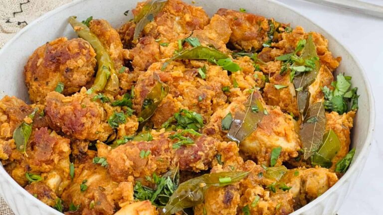 A bowl filled with pieces of fried chicken garnished with chopped herbs, green chilies, and curry leaves.