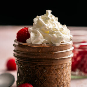 A small glass jar filled with creamy Cottage Cheese Chocolate Mousse, topped with whipped cream, and garnished with fresh raspberries.