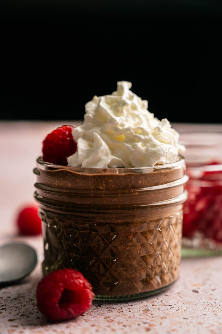 A small glass jar filled with creamy Cottage Cheese Chocolate Mousse, topped with whipped cream, and garnished with fresh raspberries.