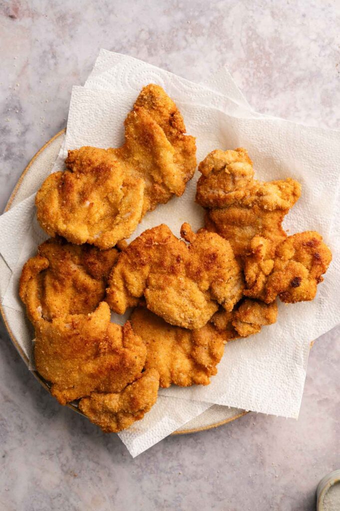 A plate lined with paper towels holds several pieces of golden-brown Crispy Chicken Thighs, each perfectly fried for a delicious crunch.