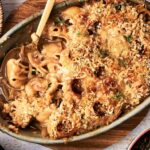 A baked Air Fryer French Onion Casserole pasta, topped with breadcrumbs and melted cheese, partially served in a ceramic dish with a wooden spoon.
