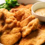 Crispy chicken thighs breaded and fried to perfection, served with a small bowl of dipping sauce, lime wedge, and fresh parsley on the side.
