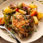 Sheet Pan Chicken Thighs and Veggies featuring roasted chicken thigh with crispy skin, served alongside mixed roasted vegetables like potatoes, green beans, and bell peppers, all garnished with fresh herbs.