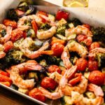 Sheet Pan Shrimp baked with cherry tomatoes, broccoli, zucchini, and red onion, all tossed in herbs and roasted together on a parchment-lined baking tray.
