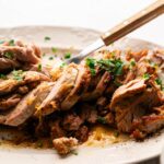 Sliced Slow Cooker Pork Tenderloin garnished with chopped parsley on a white plate, with a knife and fork nearby.