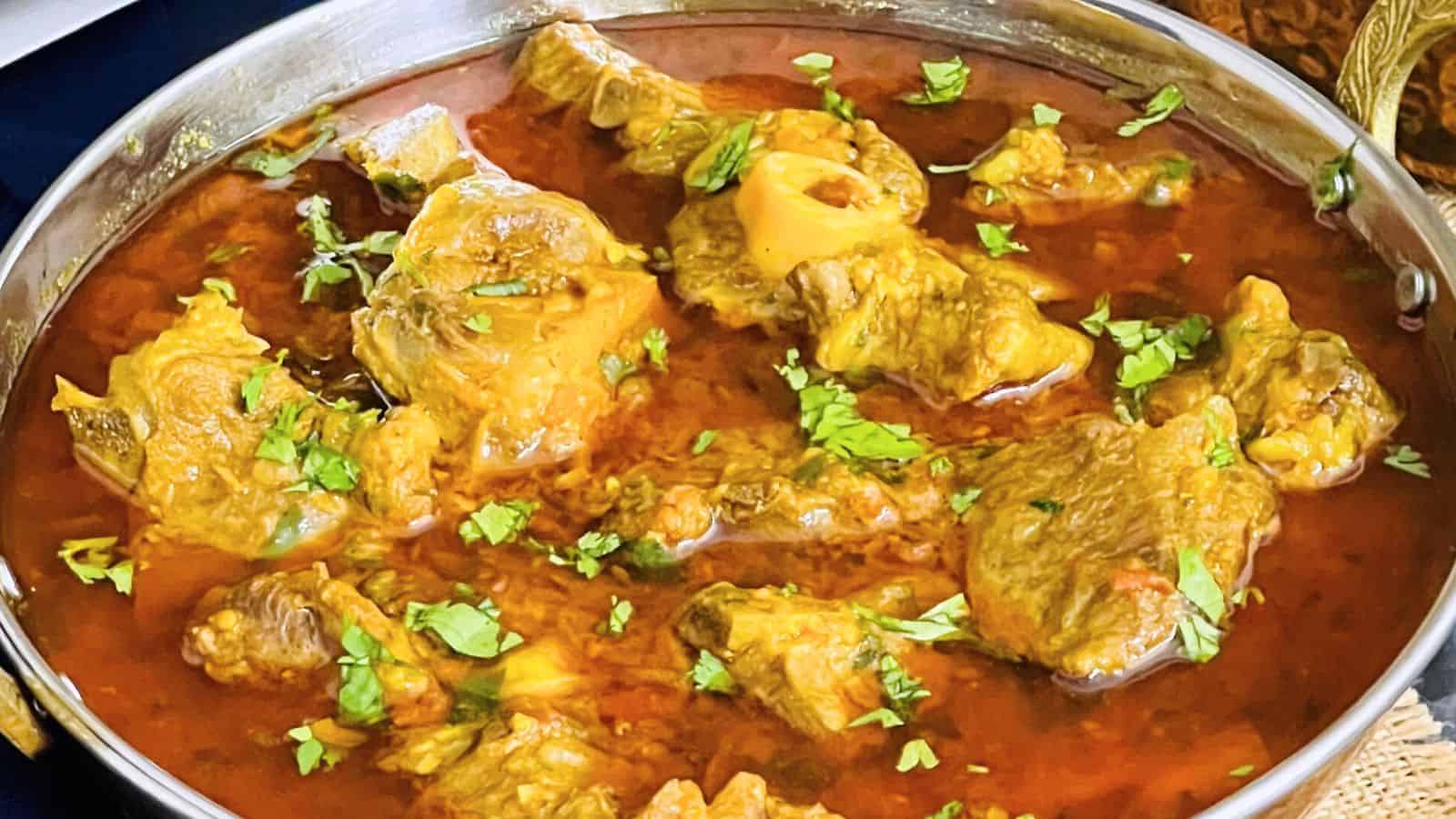 A bowl of traditional indian Lamb Curry garnished with chopped cilantro, served in a metallic dish.