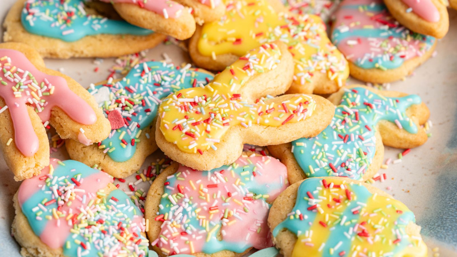 A pile of sugar cookies shaped like bunnies and other forms, decorated with pastel pink, yellow, and blue icing and topped with colorful sprinkles.