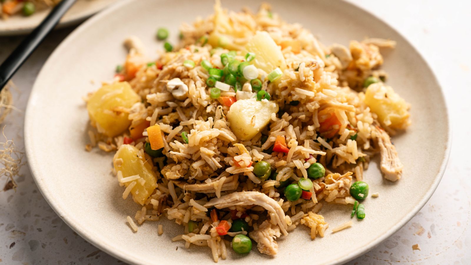 A plate of fried rice with peas, carrots, pineapple chunks, shredded chicken, and garnished with chopped green onions.