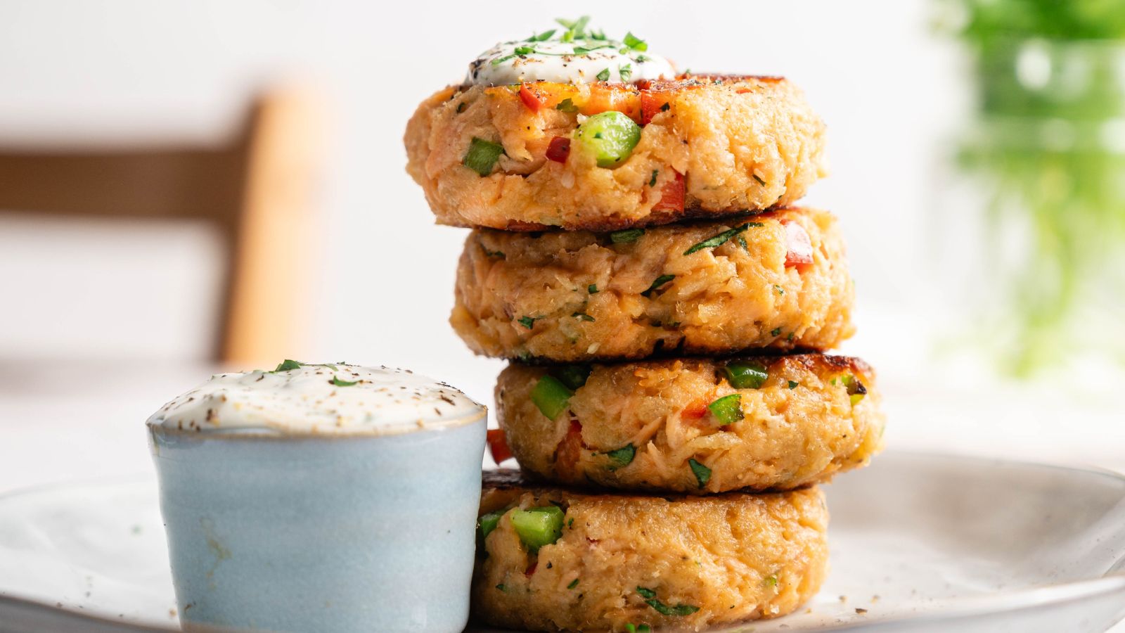 A stack of four vegetable patties is plated next to a small cup of creamy dipping sauce, garnished with herbs.
