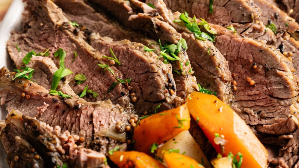 Sliced roast beef garnished with chopped herbs, served with cooked carrots and potatoes.